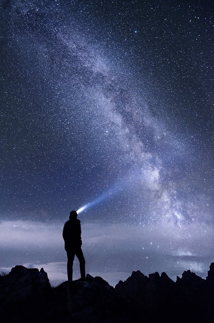 Silhouette of a person exploring the star-studded Milky Way sky at night in the mountains.